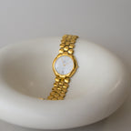 The Vintage Christian Bernard Honeycomb Gold Watch with a radiant gold finish rests elegantly on a white surface.