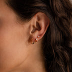 A close-up of a woman's ear with three earrings: Garnet Heart Hoops , a heart stud with heart-shaped gemstones, and a small diamond stud.