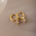 Gold Diamond Bow Hoop Earrings with delicate cubic zirconia bows, styled flat on a neutral taupe background.