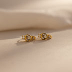 Diamond Heart Hoops: Gold heart-shaped earrings with clear stones, displayed on a soft beige surface in natural light.