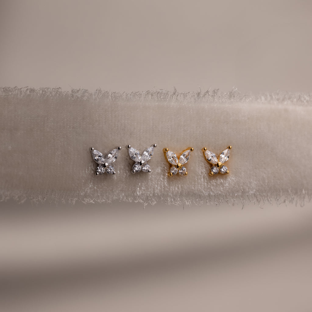 Gold and silver butterfly-shaped earrings on a beige fabric background