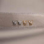 Gold and silver butterfly-shaped earrings on a beige fabric background