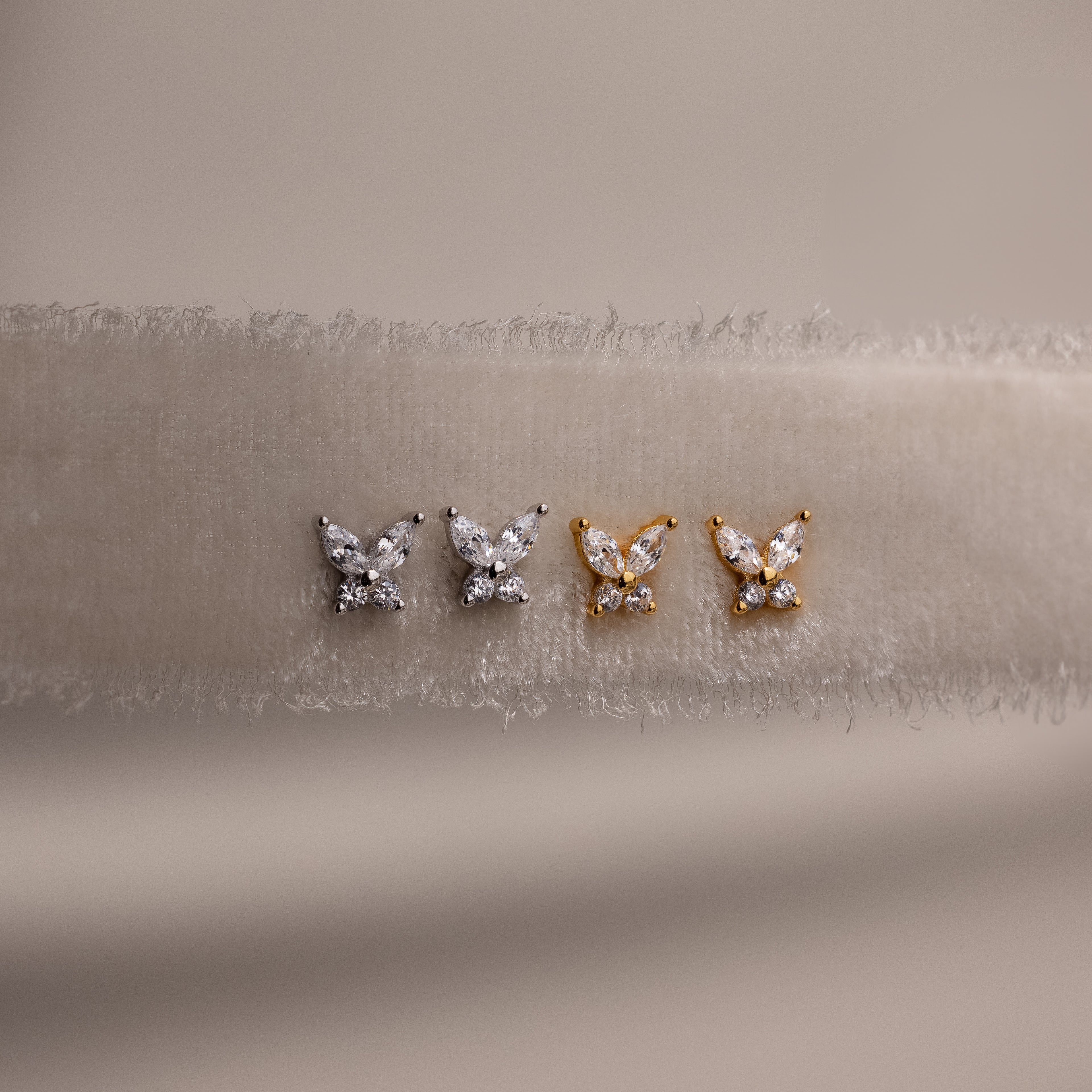 Gold and silver butterfly-shaped earrings on a beige fabric background