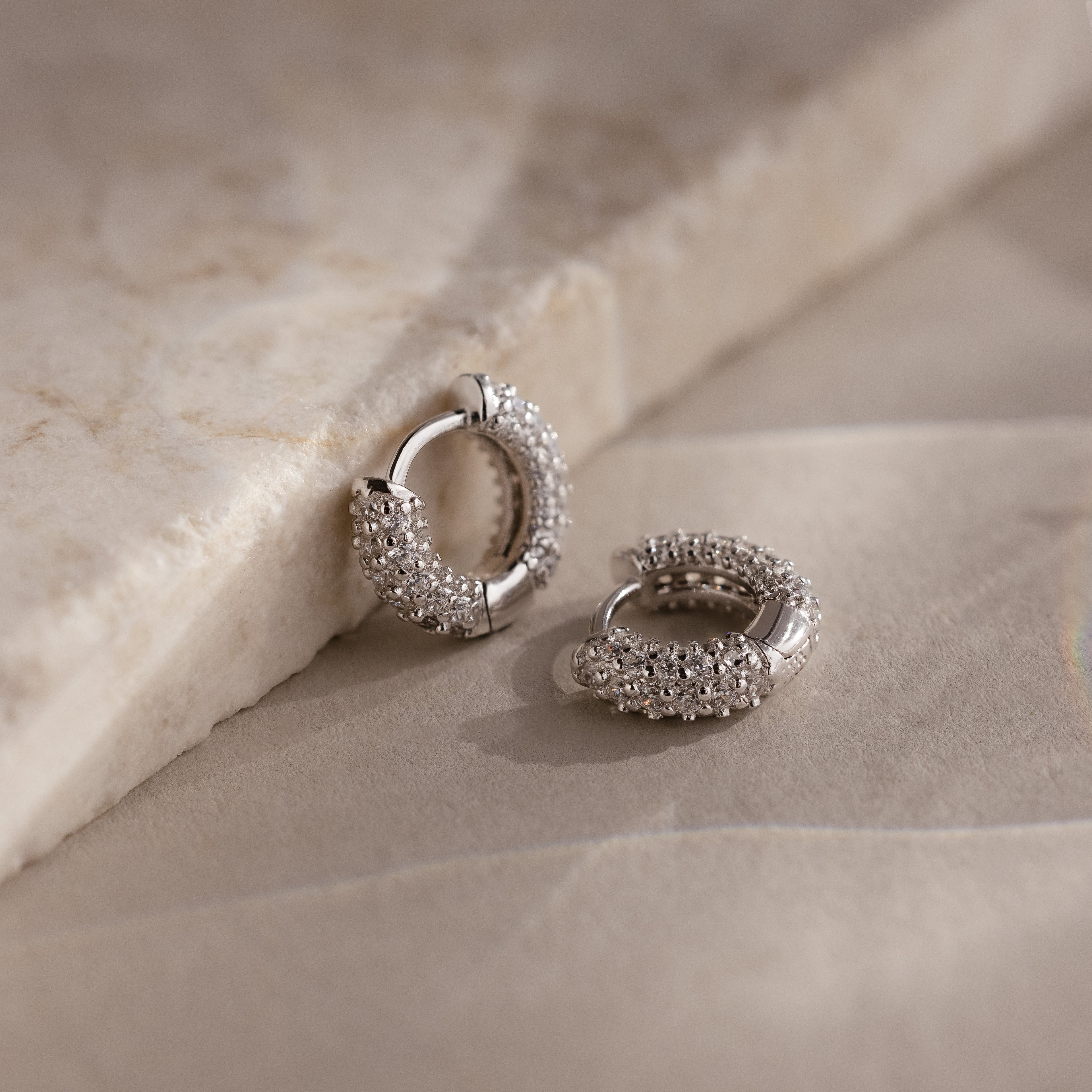 Silver hoop earrings with embedded stones on a beige stone surface