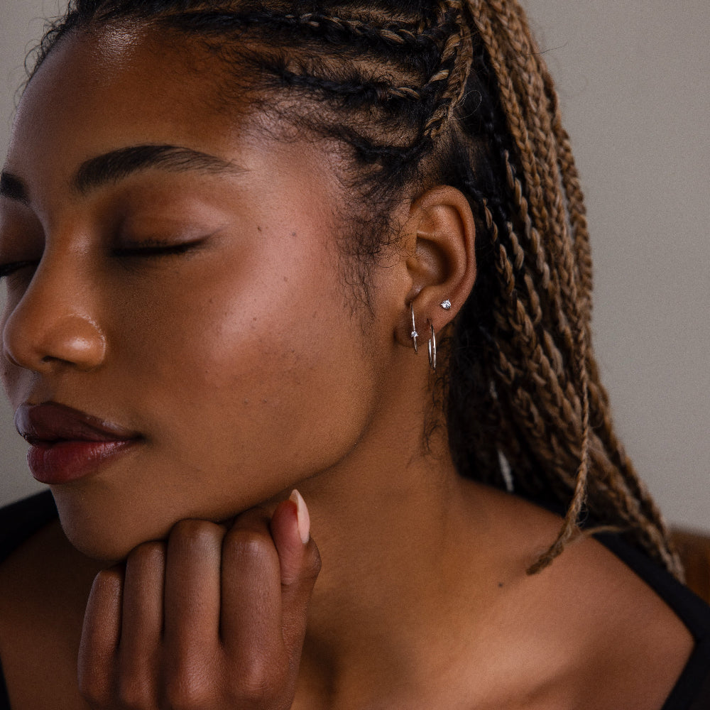 Close-up of a woman with braided hair, multiple silver earrings, and a neutral expression.