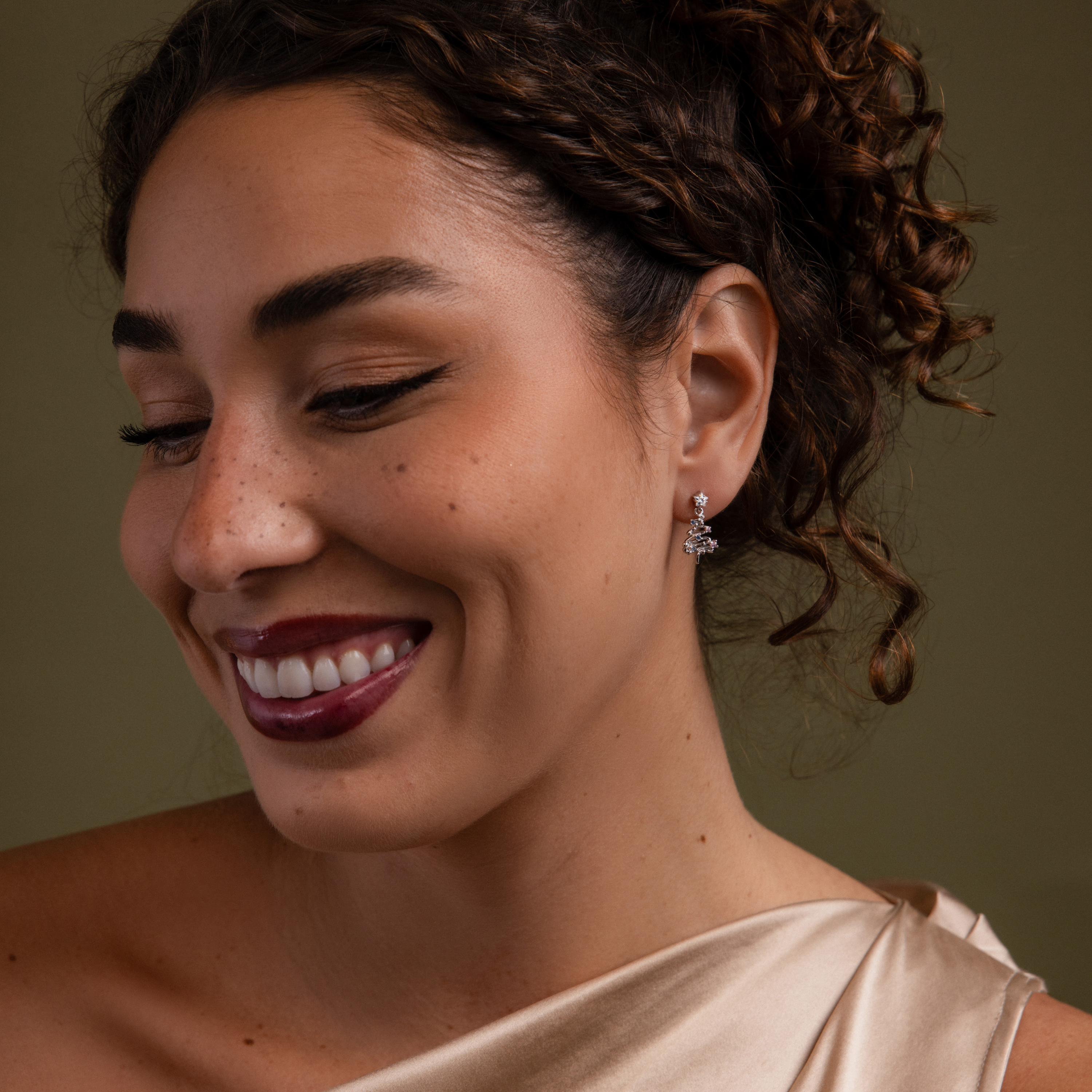 Woman with a warm smile wearing our Holiday Diamond Tree Studs against a green background