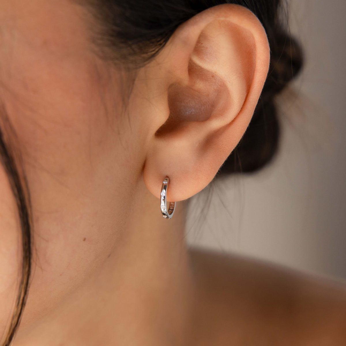 Close-up of an ear wearing a silver hoop earring with a neutral background
