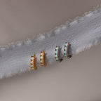 Pair of gold and silver hoop earrings with opal gemstones on a light fabric background