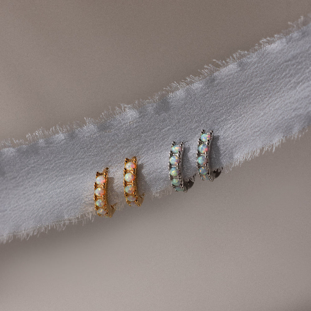 Pair of gold and silver hoop earrings with opal gemstones on a light fabric background