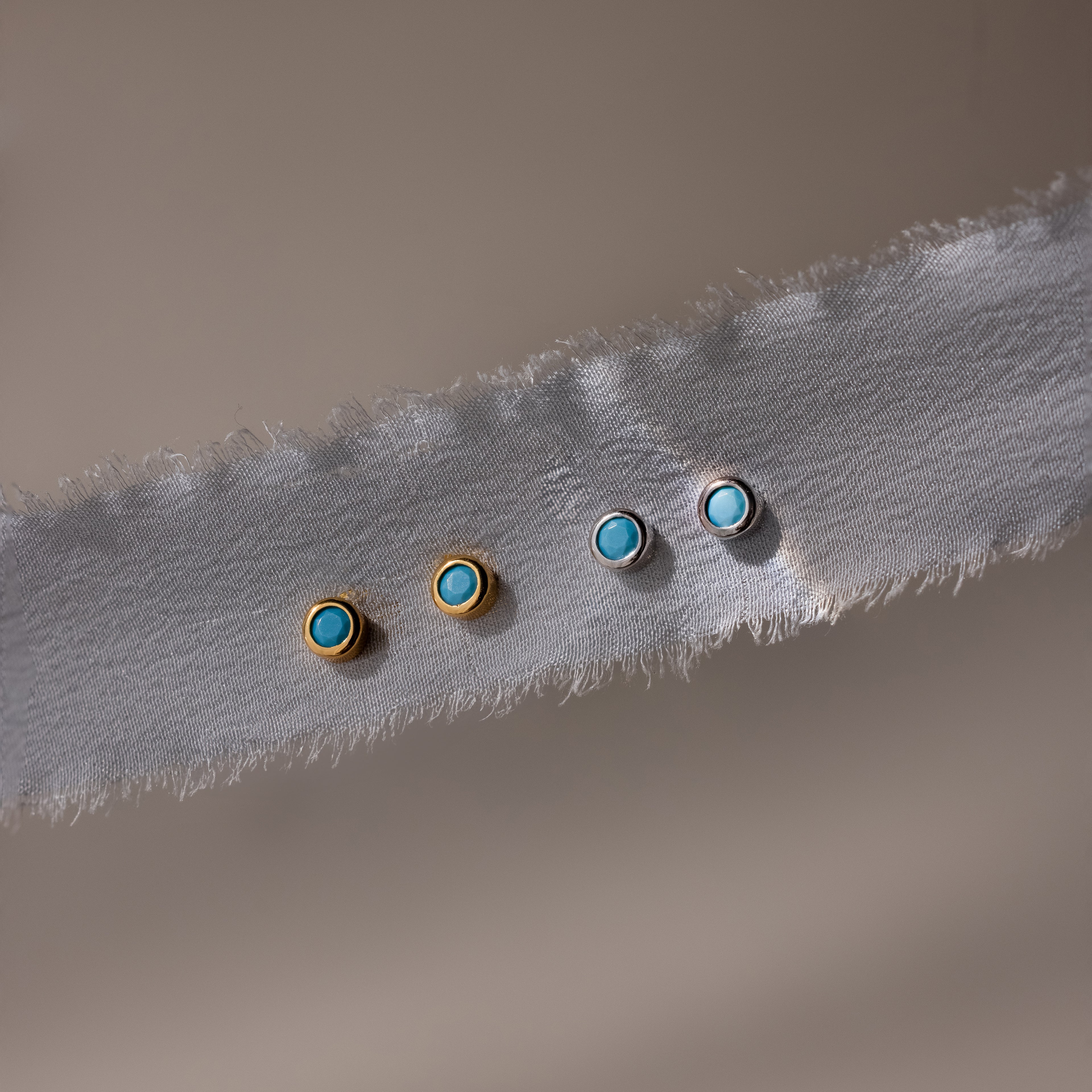 Two pairs of gold and silver earrings with turquoise stones on a textured fabric background