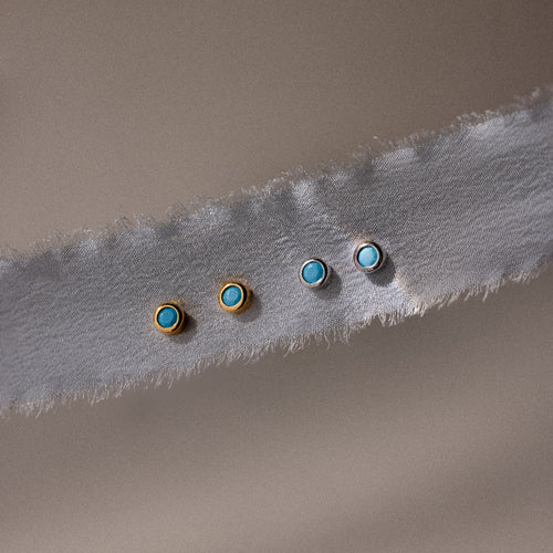 Two pairs of gold and silver earrings with turquoise stones on a textured fabric background