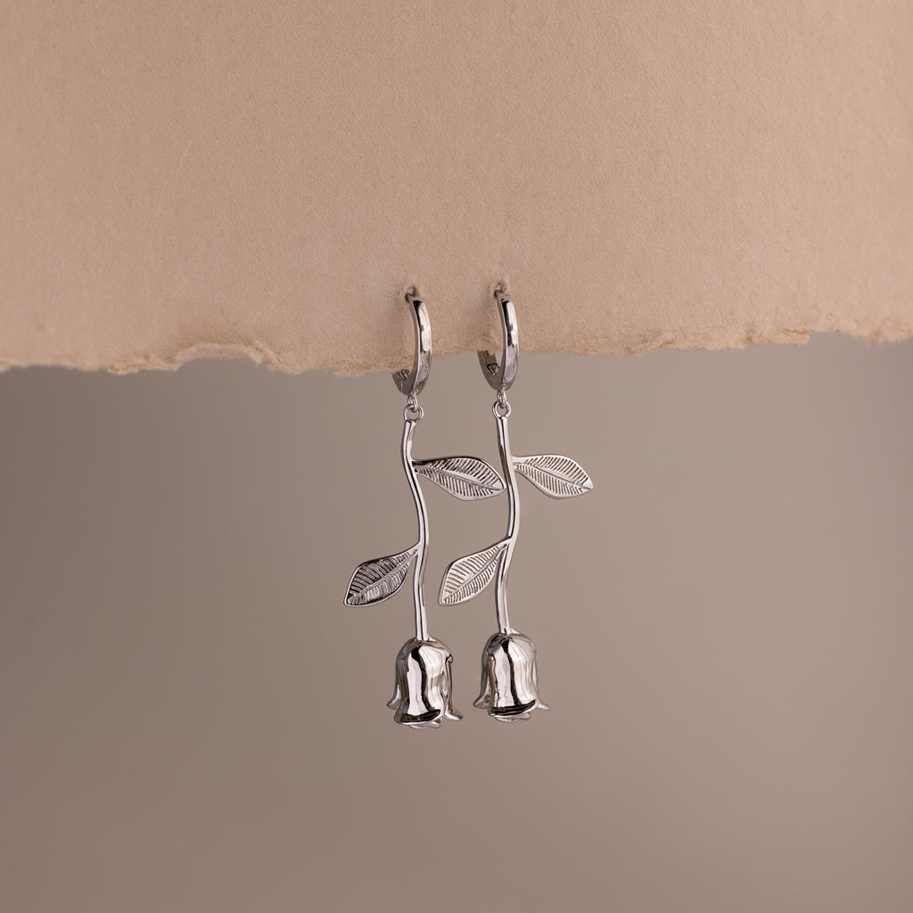 Silver earrings shaped like roses on a beige background