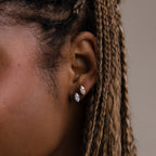 Close-up of a model with braided hair wearing two gold and silver diamond earrings against a neutral background