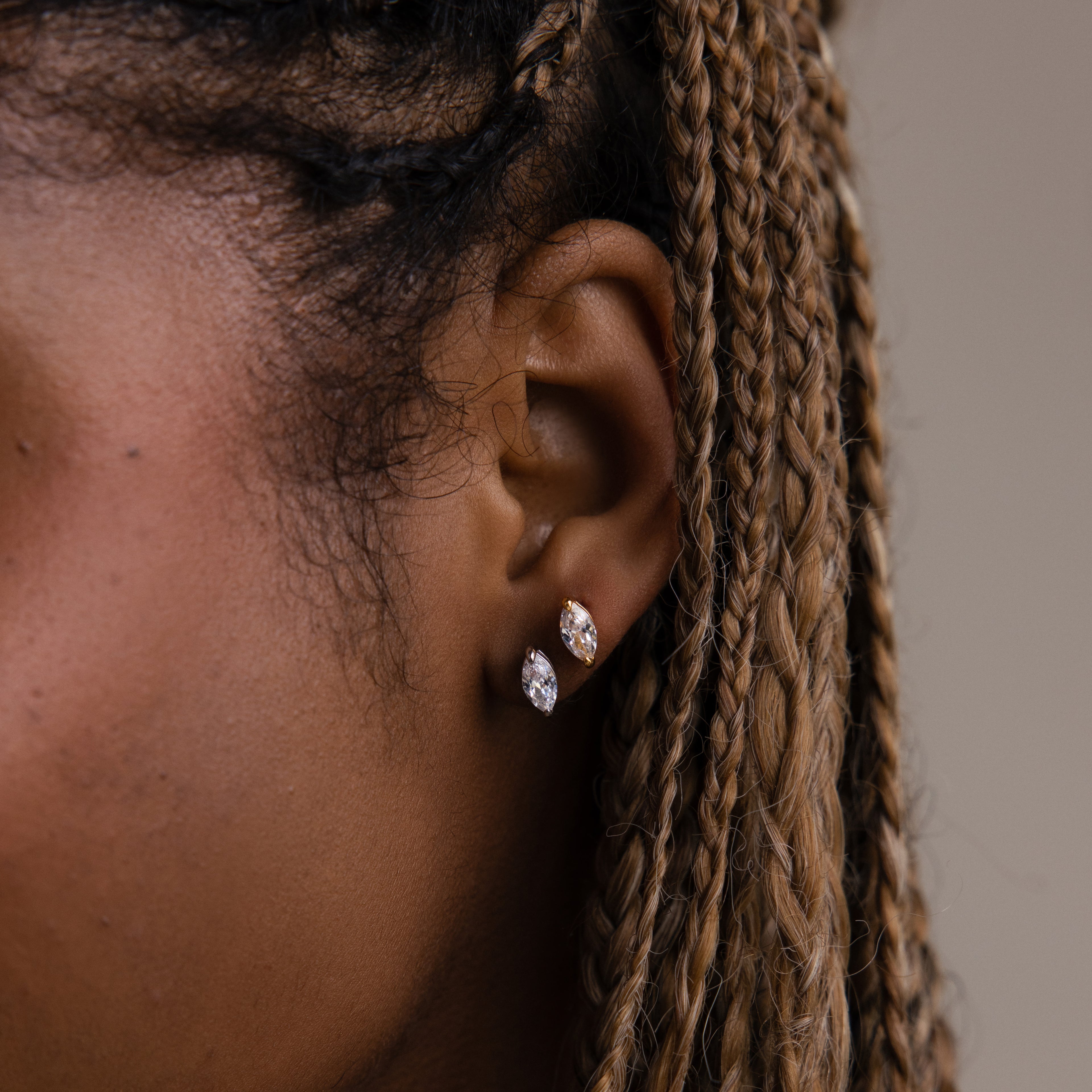 Close-up of a model with braided hair wearing two gold and silver diamond earrings against a neutral background