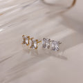 Two pairs of gold and silver stud earrings with clear gemstones on a light background