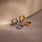 Two pairs of small hoop earrings in gold and silver on a beige surface