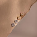 Two pairs of gold and silver diamond earrings on a beige fabric surface