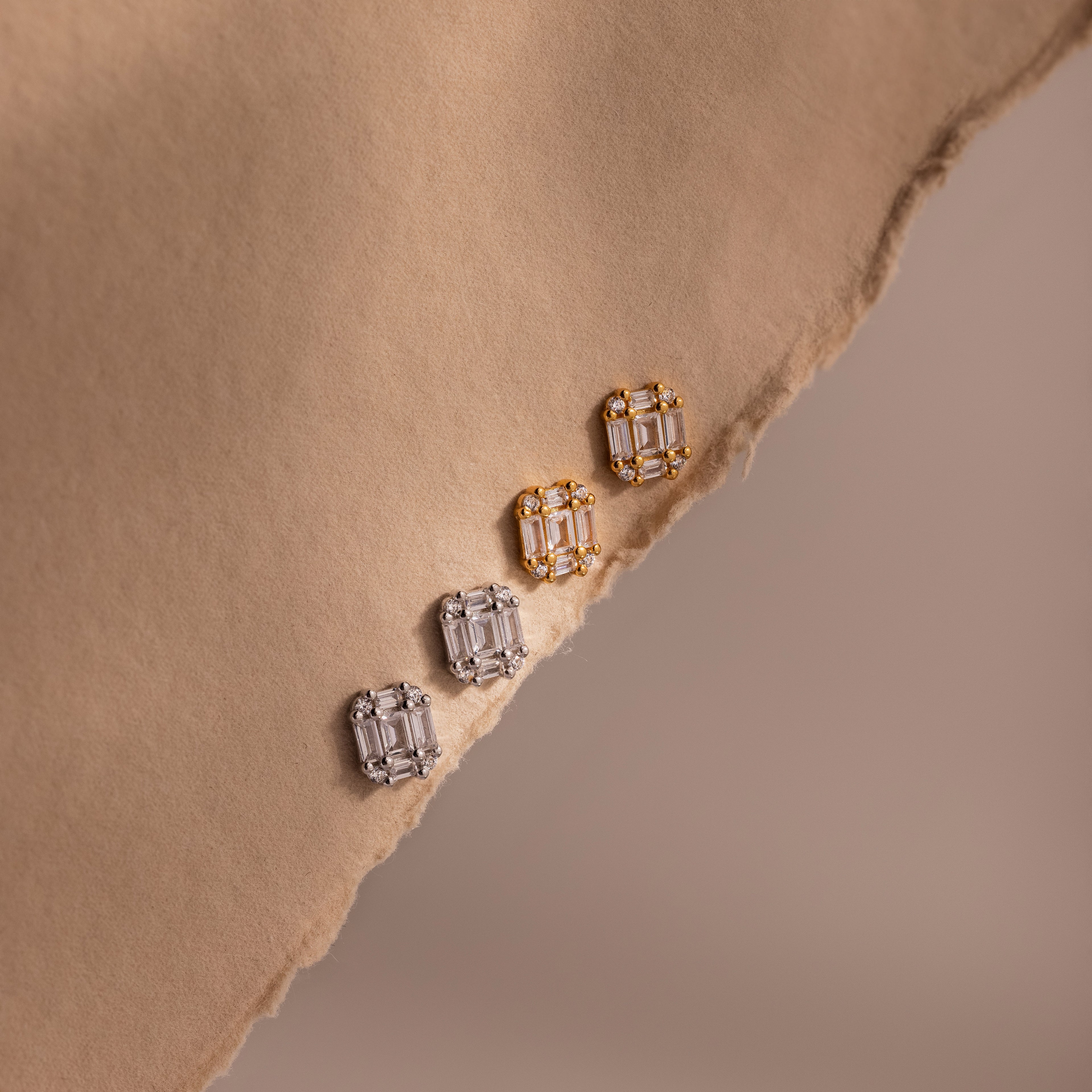 Two pairs of gold and silver diamond earrings on a beige fabric surface