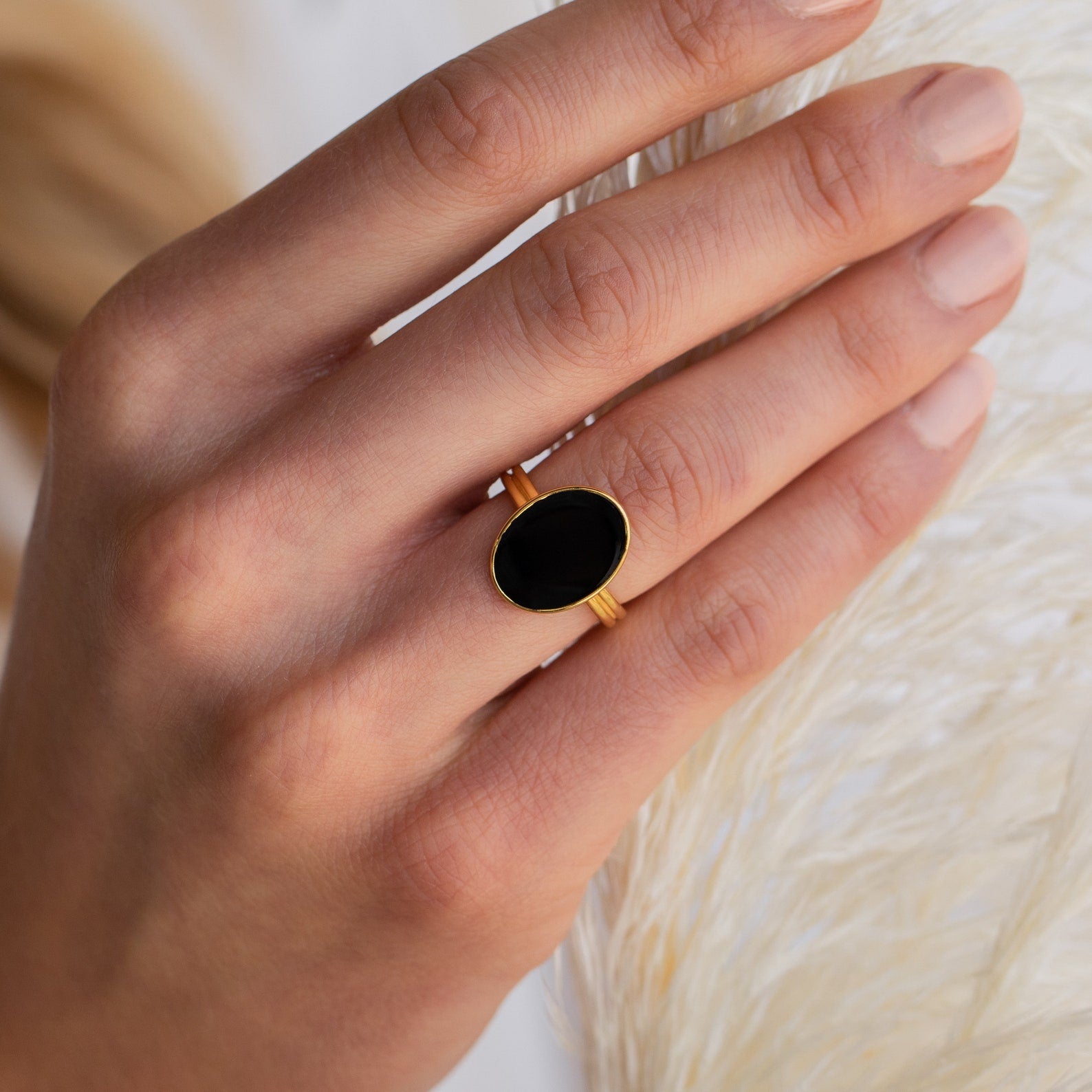 A hand wearing the Midnight Hour Onyx Ring with an adjustable band, fingers resting on a softly textured surface.