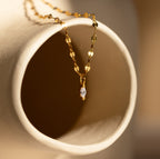 The Dainty Marquise Pendant Necklace drapes elegantly over a curved beige ceramic surface, highlighting its marquise-cut diamond charm on a delicate mirror twist chain.