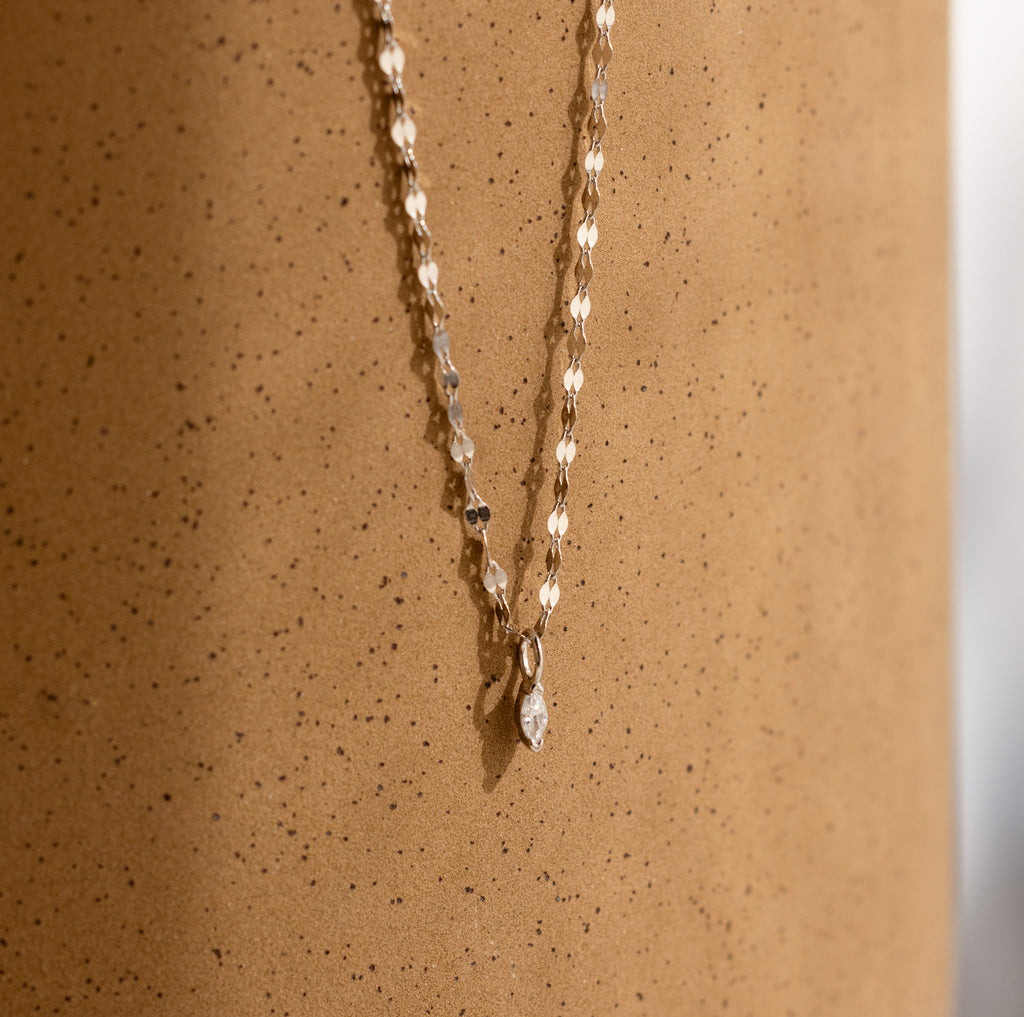 Dainty Marquise Pendant Necklace in Silver with a mirror twist chain, displayed elegantly against a speckled, light brown cylindrical surface.