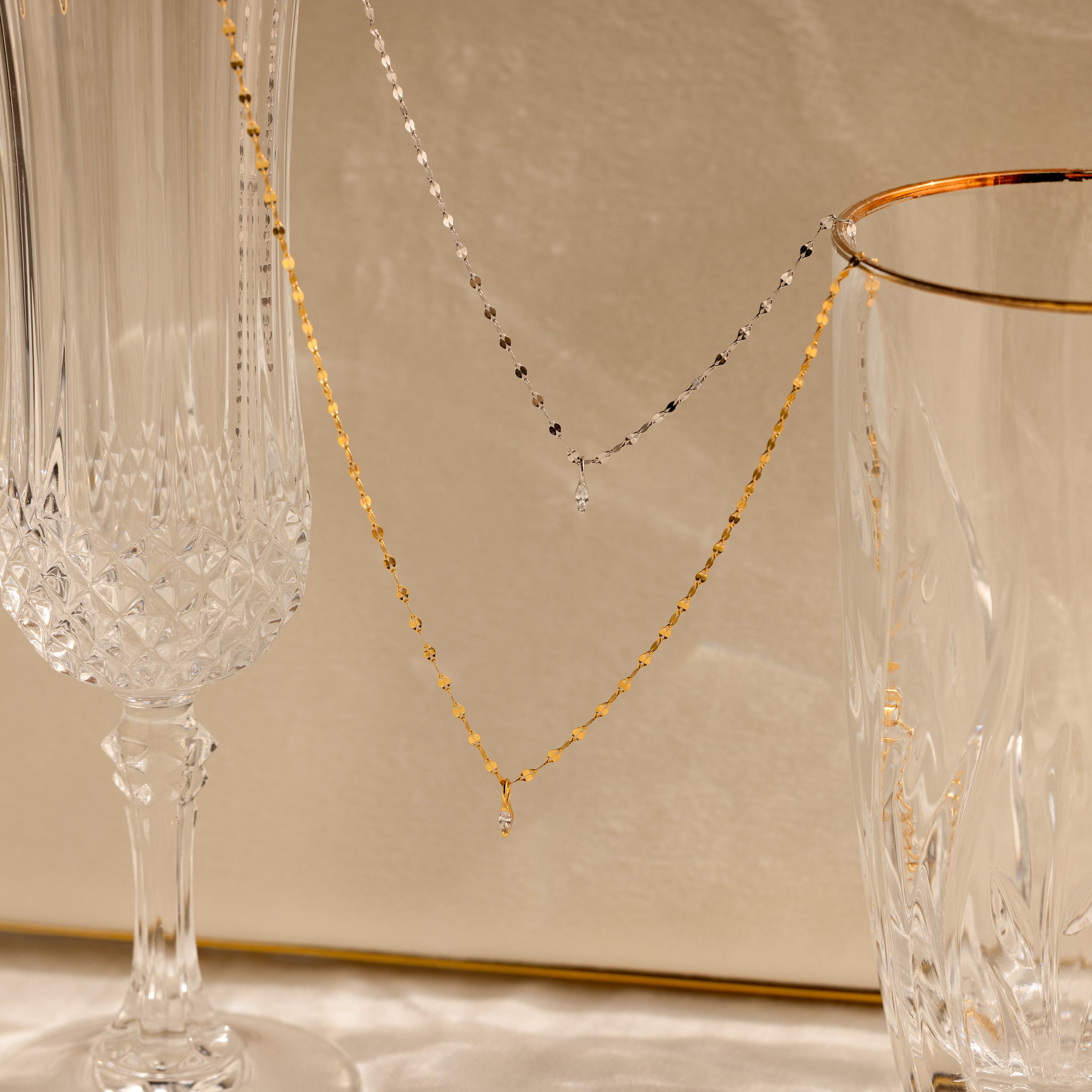 The Dainty Marquise Pendant Necklace is draped over two crystal glasses with a soft beige background.