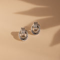 Silver Mini Triple Knot Earrings lie on a smooth beige surface