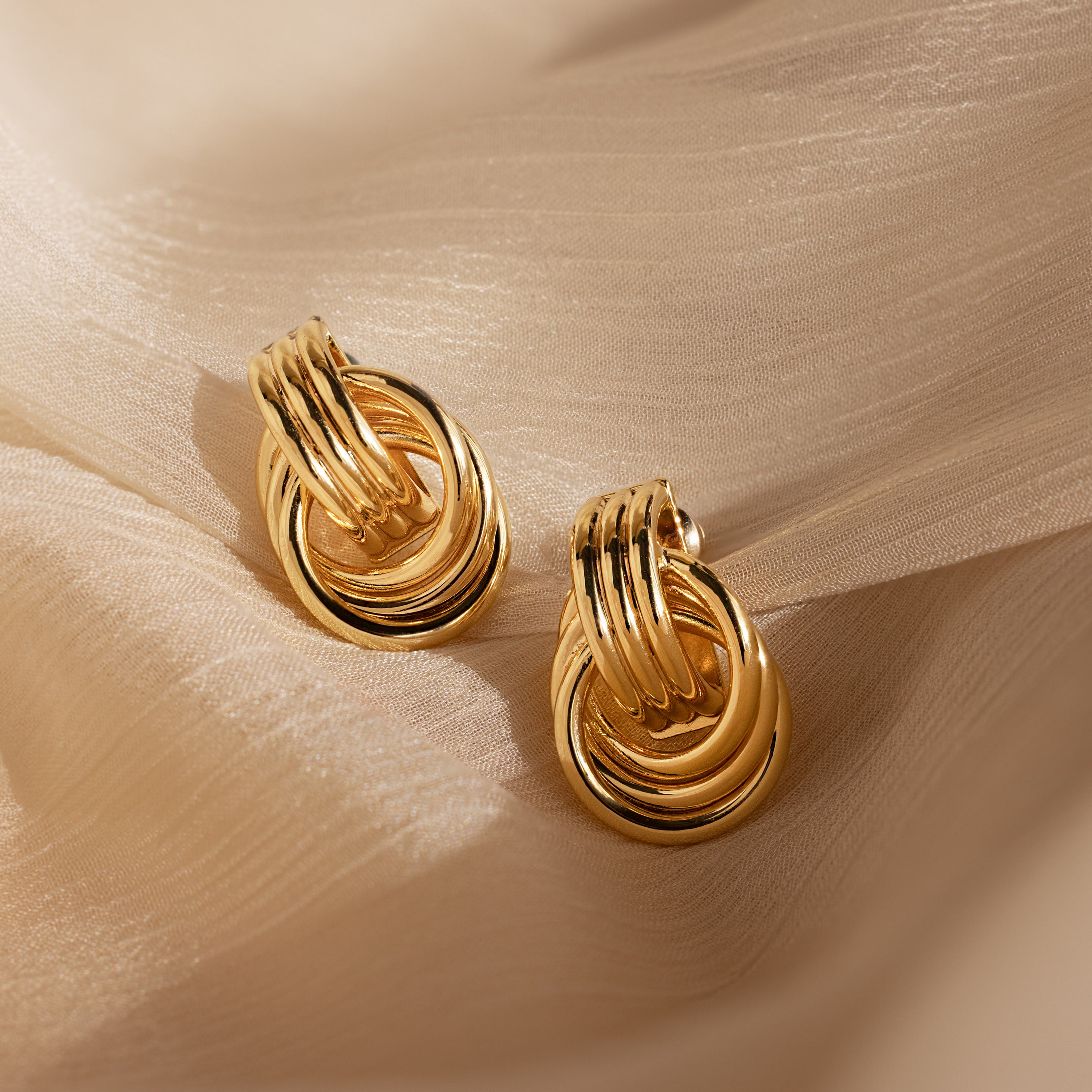 Triple Knot Earrings with interlocking circles, shown on soft beige fabric under gentle lighting—an elegant choice and perfect anniversary gift.