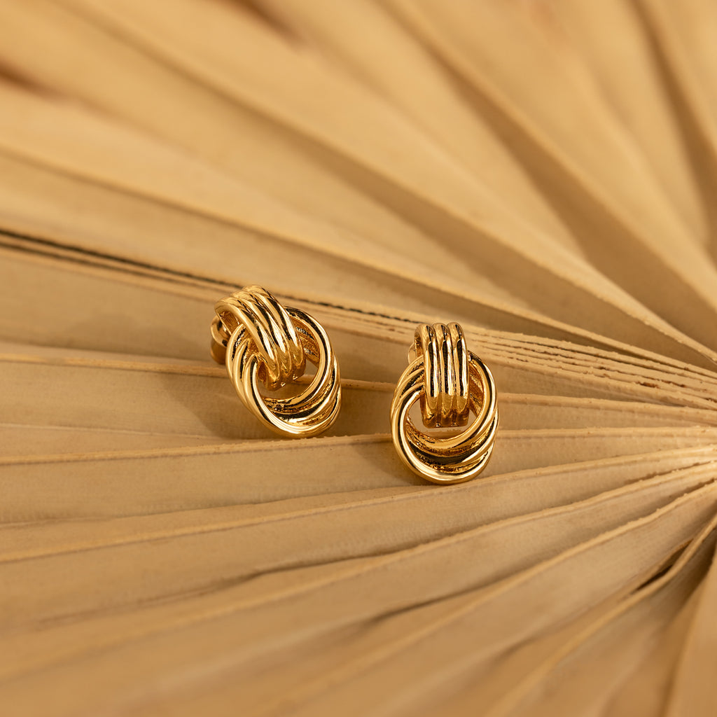 Pair of Mini Triple Knot Earrings styled on the folds of a tan paper fan, showcasing their shiny gold finish.