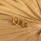 Pair of Mini Triple Knot Earrings styled on the folds of a tan paper fan, showcasing their shiny gold finish.