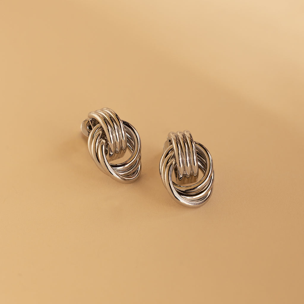 Silver Mini Triple Knot Earrings resting on a beige surface.