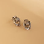 Silver Mini Triple Knot Earrings resting on a beige surface.
