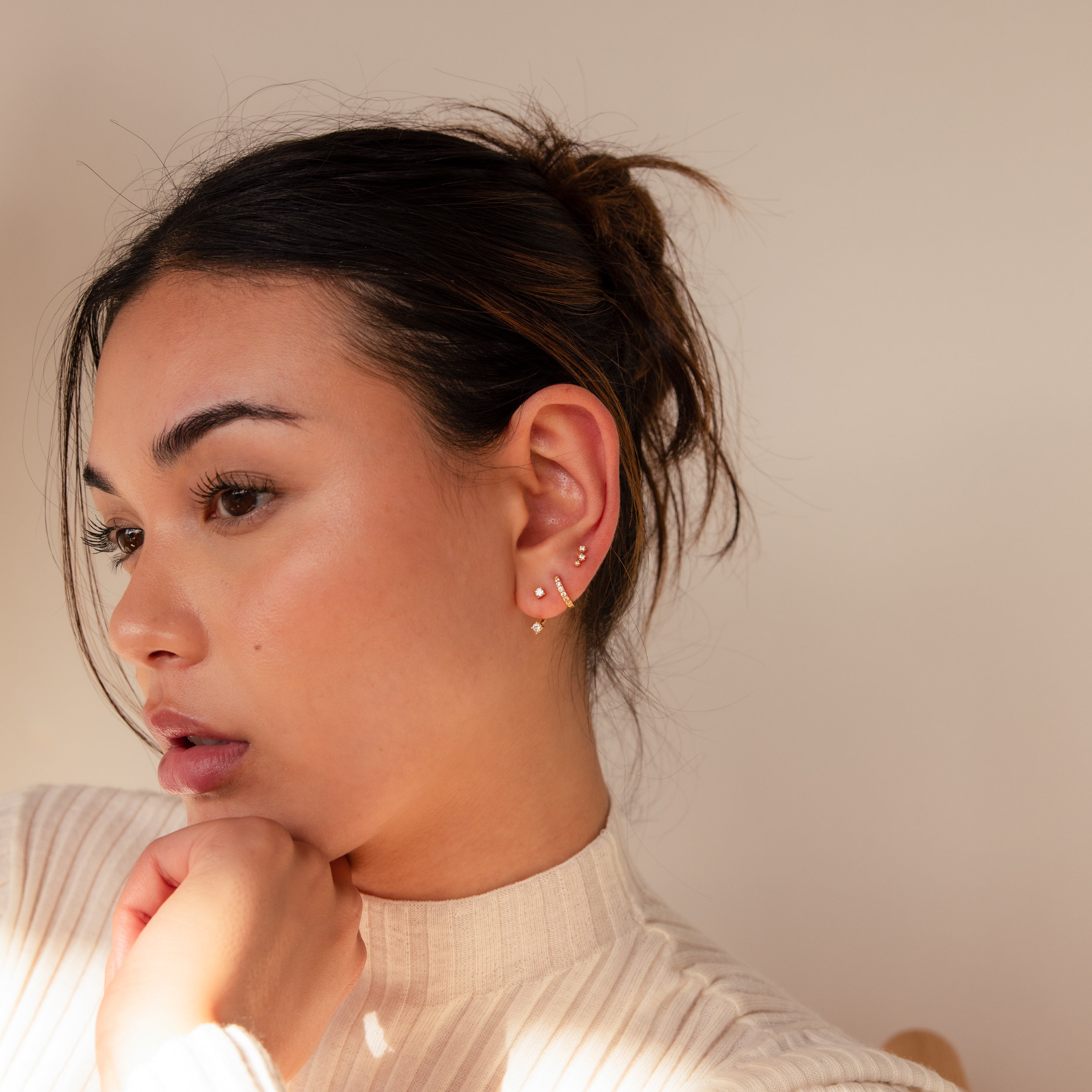 A woman with dark hair in a bun, wearing the Diamond Earrings Set, looks thoughtful with her hand on her chin.