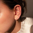 Close-up of a woman's ear wearing the Diamond Earrings Set in 18K Gold, featuring sparkling pavé huggie hoops and delicate studs styled in multiple piercings.
