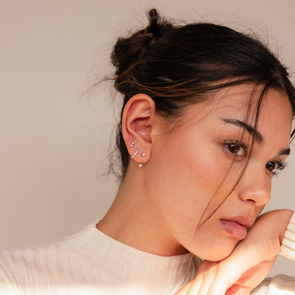Woman with dark hair in a bun, wearing the Diamond Earrings Set in Sterling Silver, rests her face on her hand.
