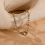 The Rolo Circle Charm Bracelet in White Gold features a detachable hinged circle, ideal for adding your own charms or achieving a minimalist style—shown on a textured, neutral-toned surface.