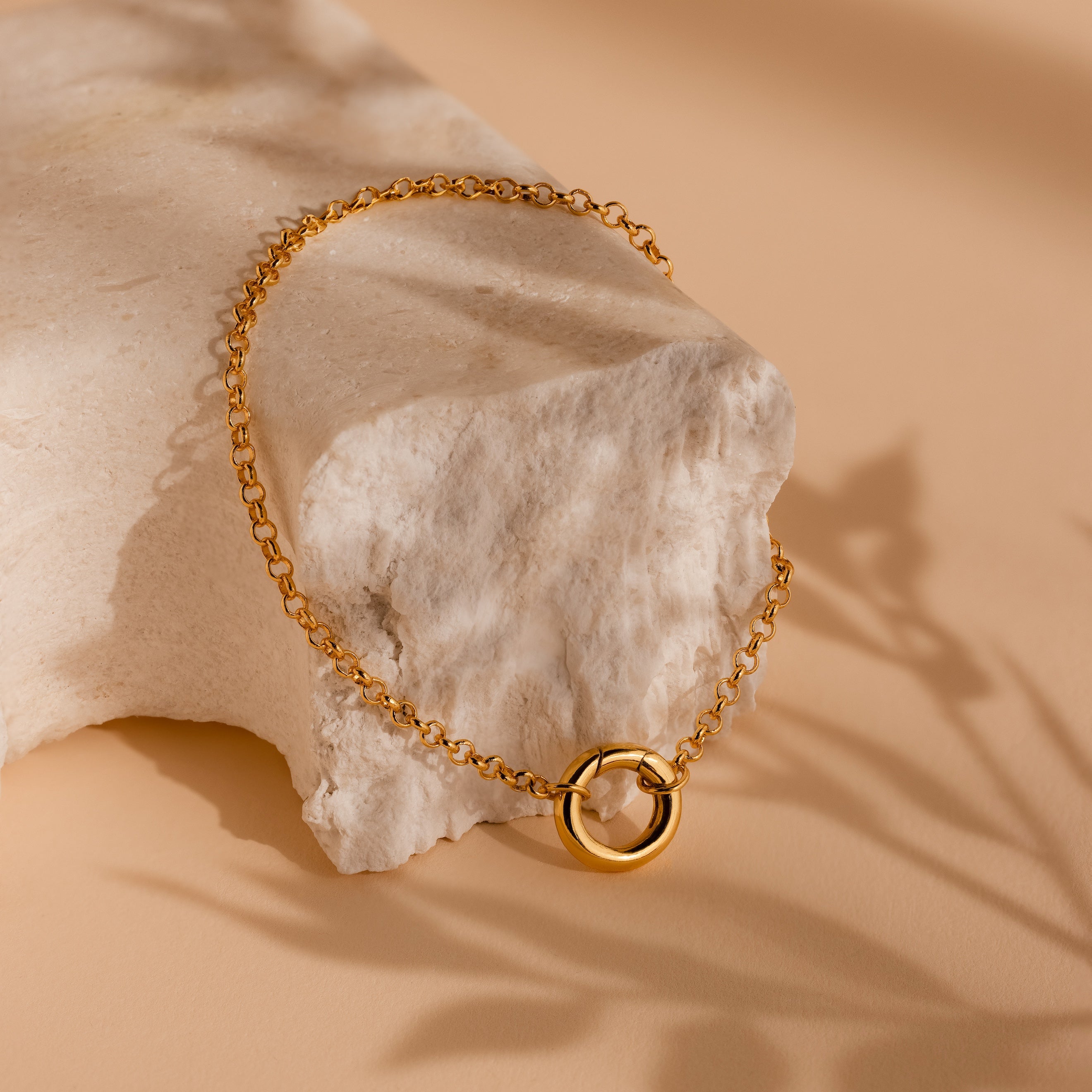 A Rolo Circle Charm Bracelet draped over a textured, light stone on a beige surface.