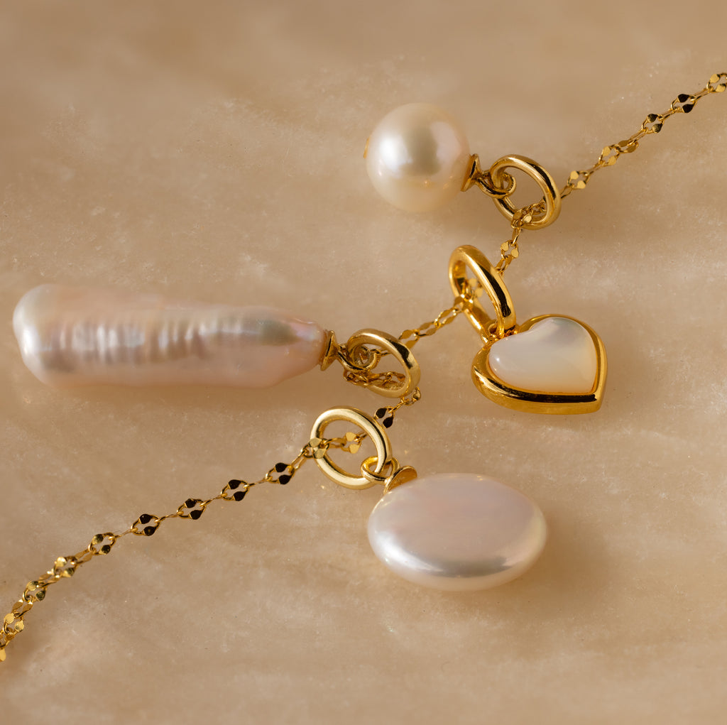 Round Pearl Charm necklace featuring a heart pendant, Mother of Pearl pendant, and round pearl charms displayed on a marble surface.