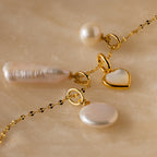 Round Pearl Charm necklace featuring a heart pendant, Mother of Pearl pendant, and round pearl charms displayed on a marble surface.