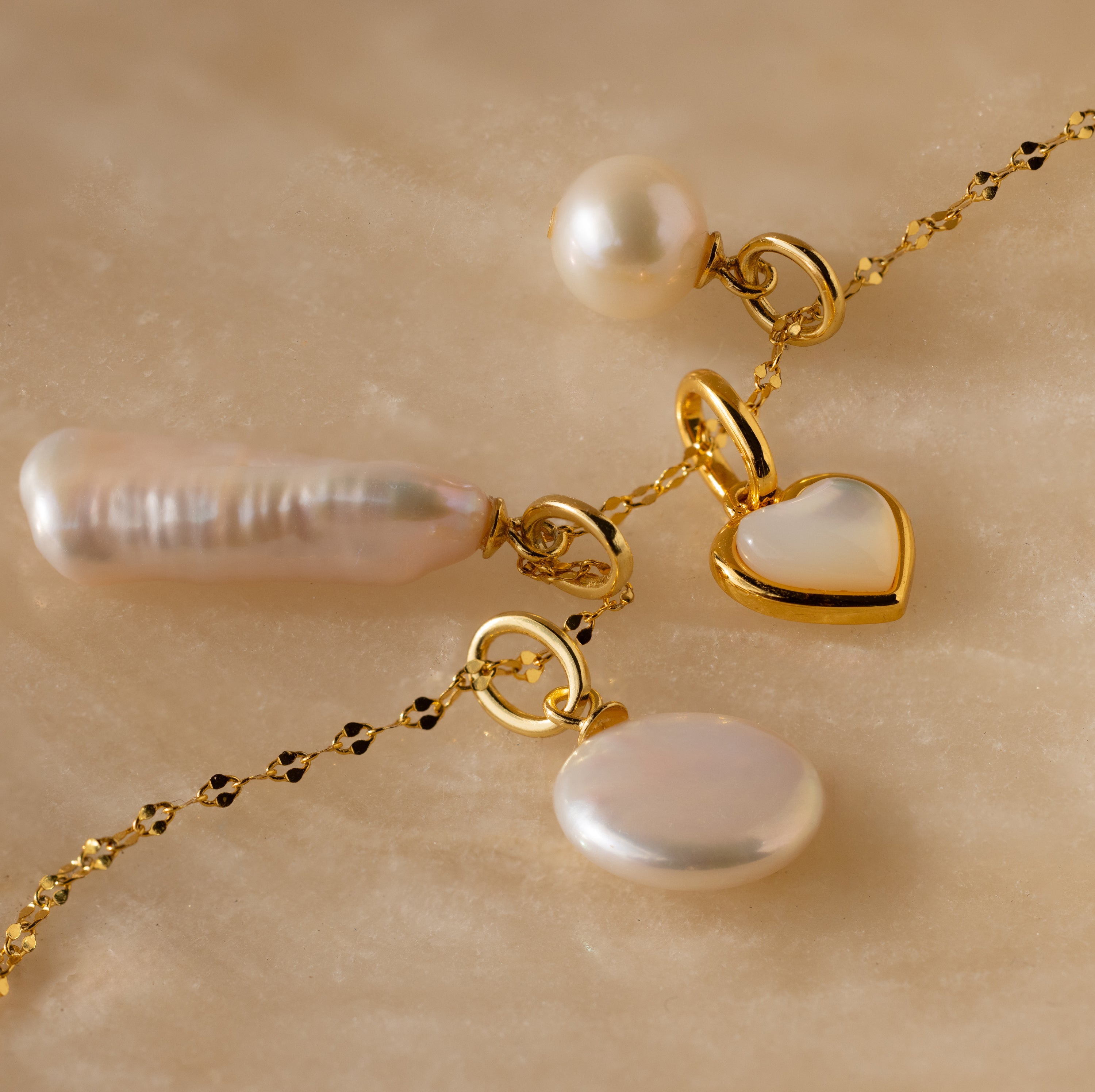 Round Pearl Charm necklace featuring a heart pendant, Mother of Pearl pendant, and round pearl charms displayed on a marble surface.