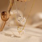 The Interlocking Pearl Necklace, featuring circular pendants and beaded pearl charms, is elegantly displayed on sand and glass.