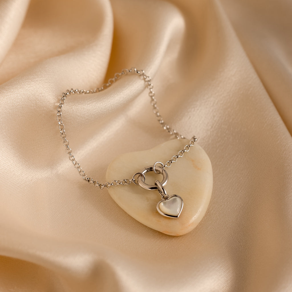 Silver heart pendant necklace on cream-colored stone, resting on beige satin. Pair it with our Rolo Circle Charm Bracelet in White Gold or add charms for a personalized, elegant style.