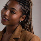 Woman with braided hair wearing a silver hoop earring and a brown pinstripe blazer against a neutral background