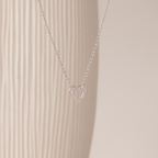 The Rolo Heart Clasp Necklace in White Gold features a delicate open heart pendant on a classic rolo chain, shown against a neutral textured background.