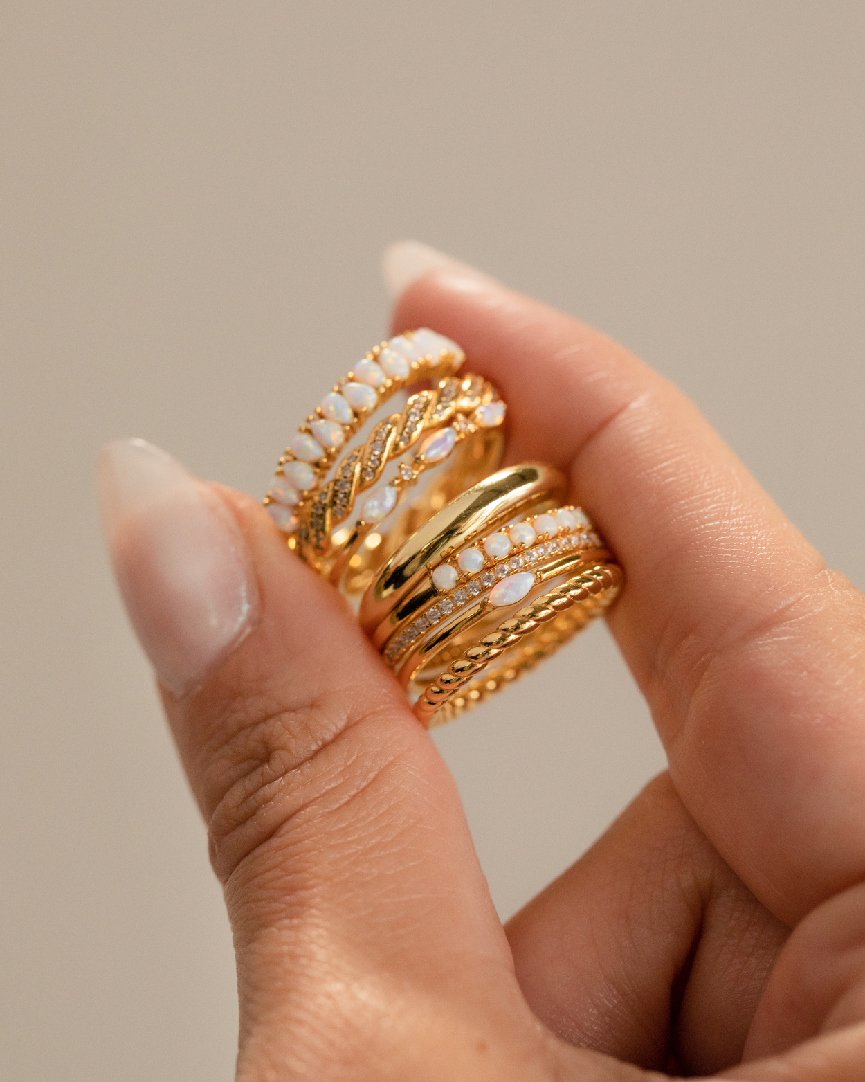 A ring jewelry collection feature photo of a jewelry model holding a set of gold rings in this order: opal eternity ring, twisted diamond ring, opal marquise ring, bold dome ring, crescent opal ring, marquise opal signet ring and twisted gold ring.