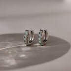Pair of silver hoop earrings with opal gemstones on a marble surface