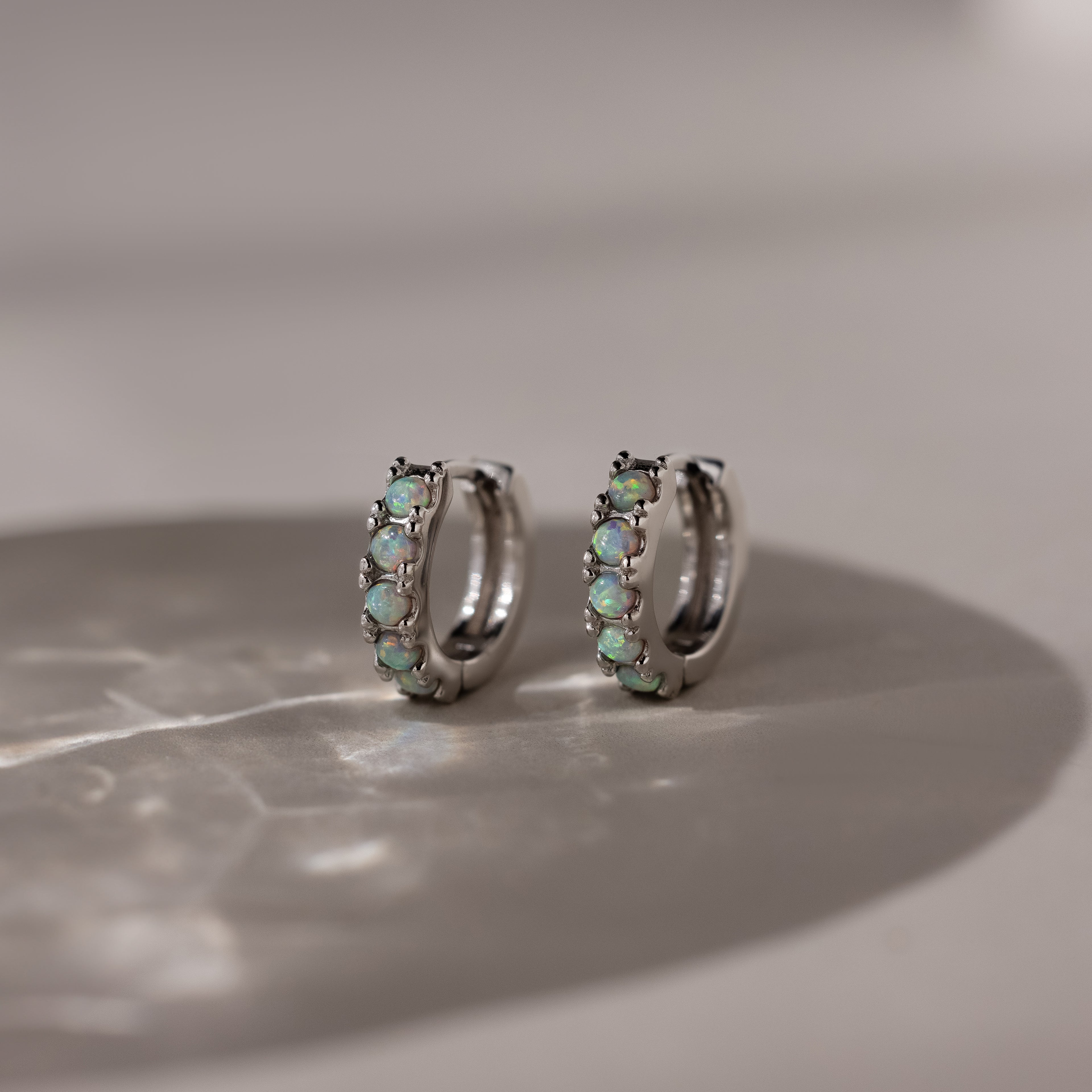 Pair of silver hoop earrings with opal gemstones on a marble surface