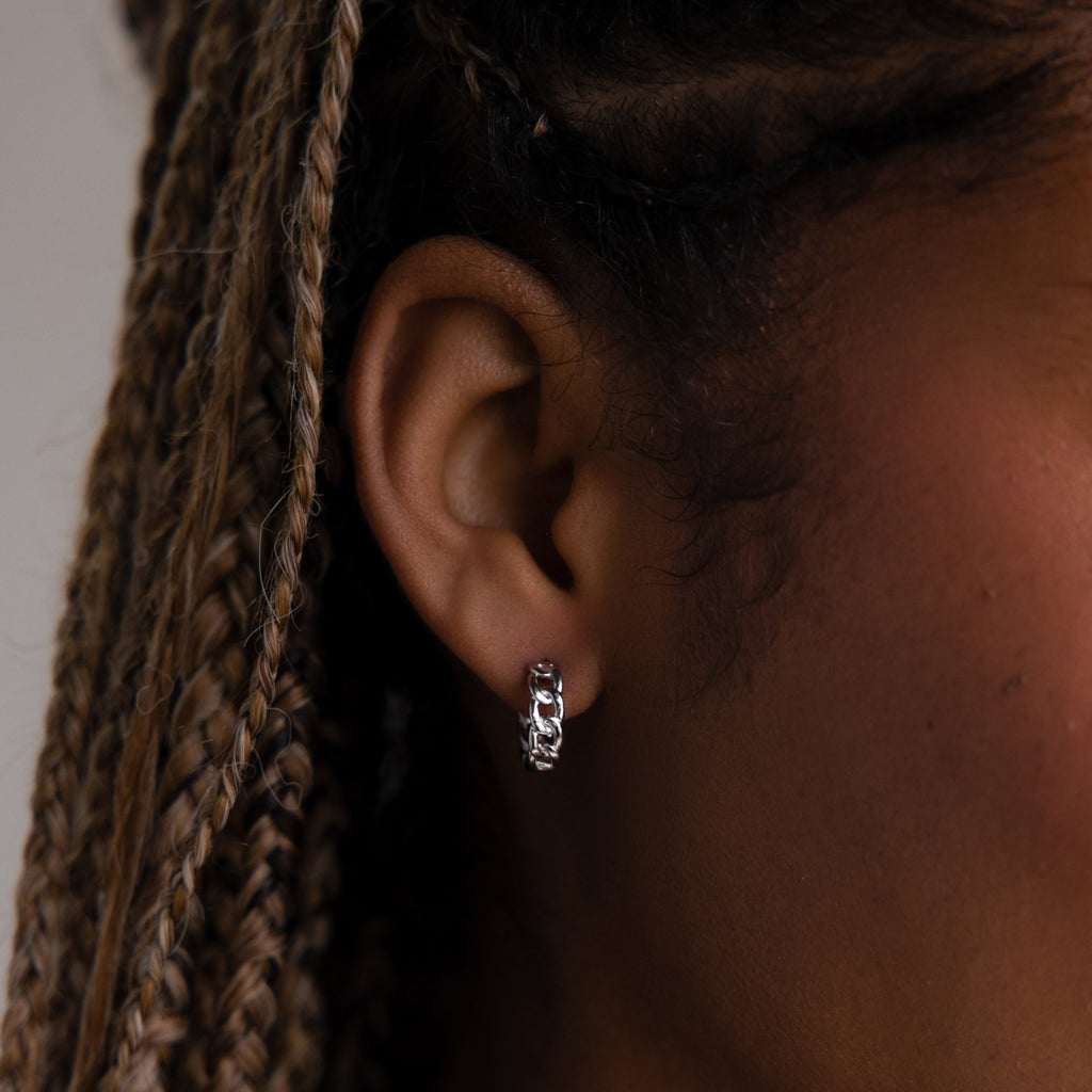 Close-up of a model wearing a silver chain hoop earring with braided hair.