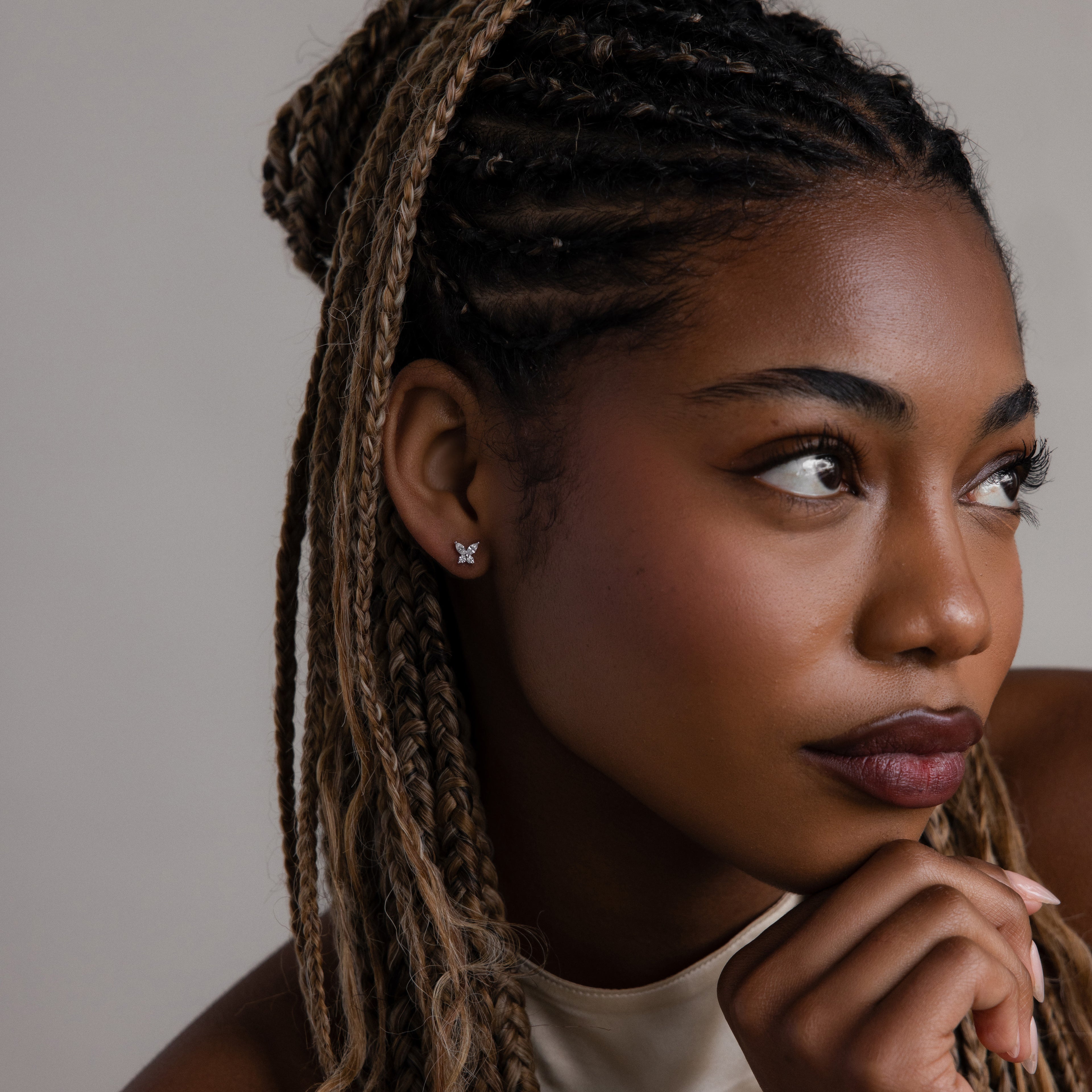 Woman with braided hair wearing a diamond butterfly shaped earring against a neutral background