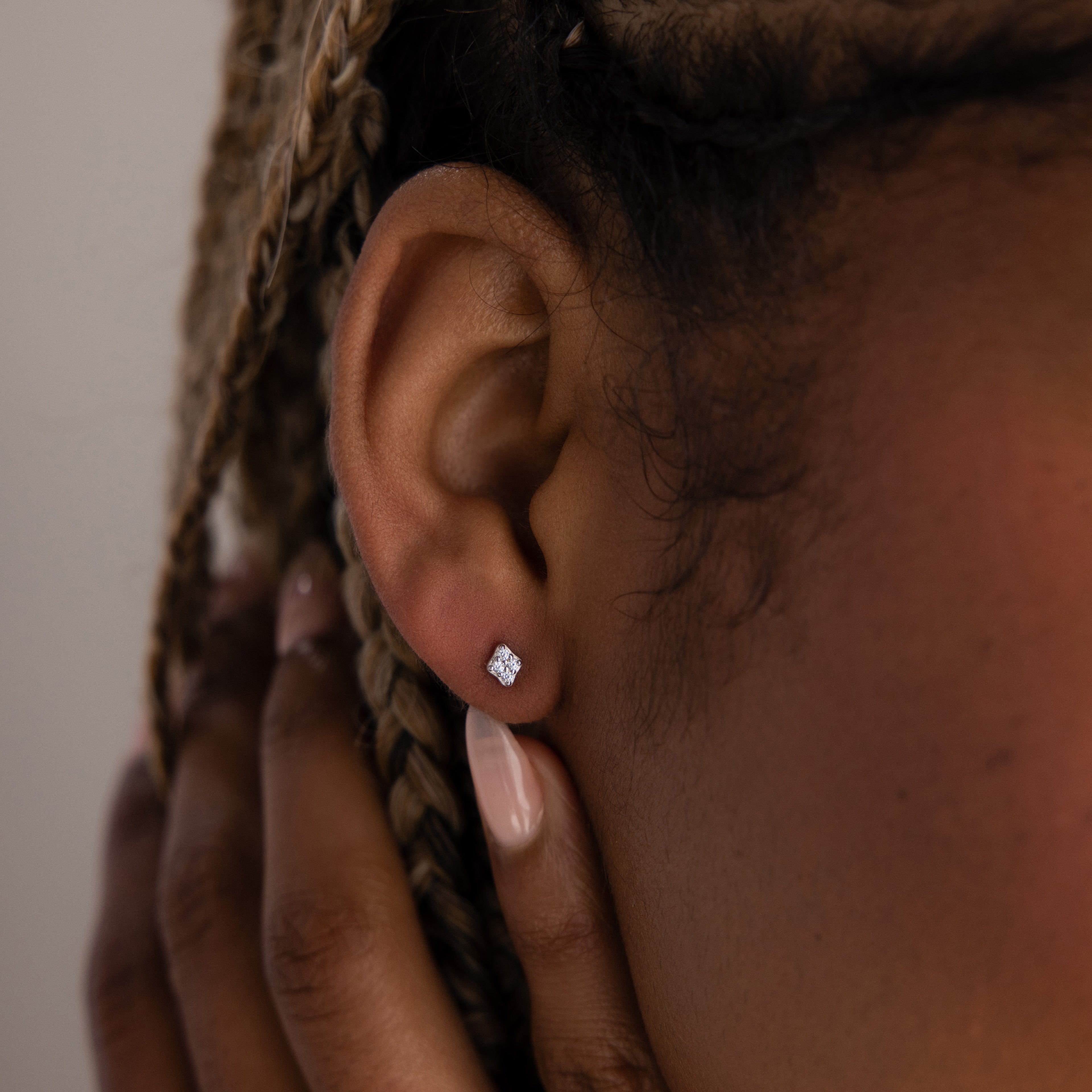 Close-up of a model with a silver diamond earring, hand brushing gently against face.